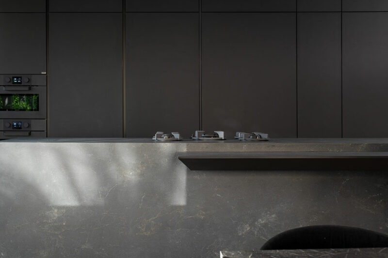 La moderna cocina minimalista cuenta con gabinetes oscuros mate, hornos dobles empotrados, encimeras de piedra lisa y tres quemadores de gas en la isla.