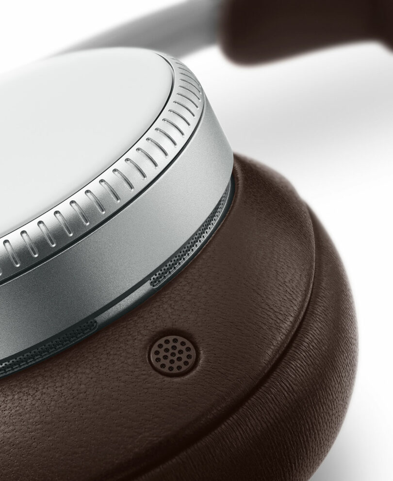 Close-up of a headphone ear cup featuring a metallic ring, a brown leather cushion, and a small built-in microphone.
