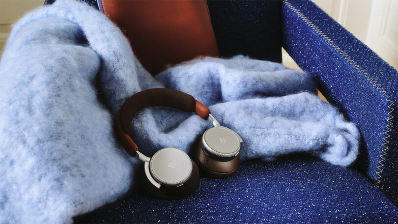 A pair of over-ear headphones rests on a fluffy blue blanket draped over a blue upholstered armchair.