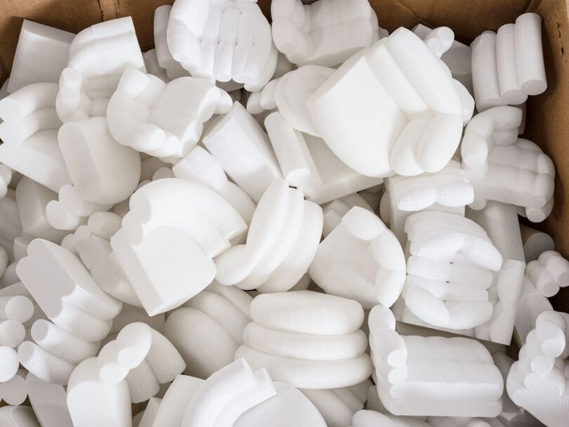 Una caja está llena de numerosos objetos de plástico blanco impresos en 3D con forma de puños y manos cerrados.