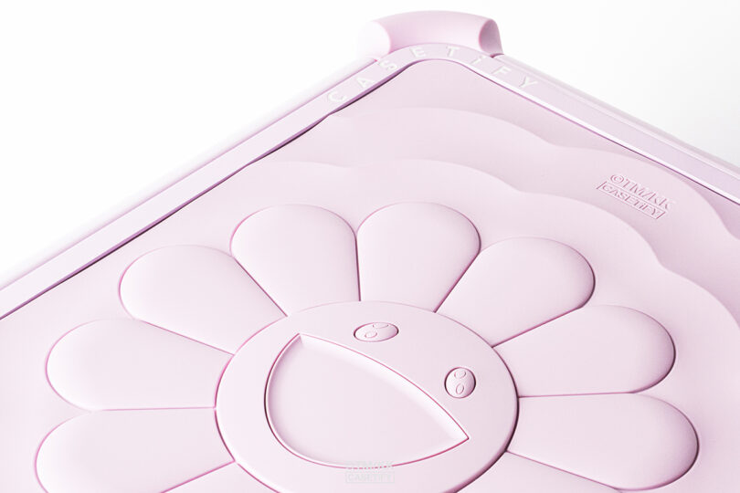 Primer plano de la funda para teléfono CASETiFY de color rosa pálido con un diseño de flor sonriente en relieve y una cara estilizada.