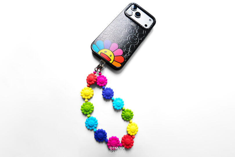 Smartphone en funda negra con diseño de flores sonrientes de colores y viene con una cadena de cuentas de flores de colores desmontable.