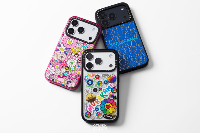 Tres smartphones con carcasas con motivos florales estilo Murakami en rosa, azul y diseños transparentes dispuestos sobre una superficie blanca.