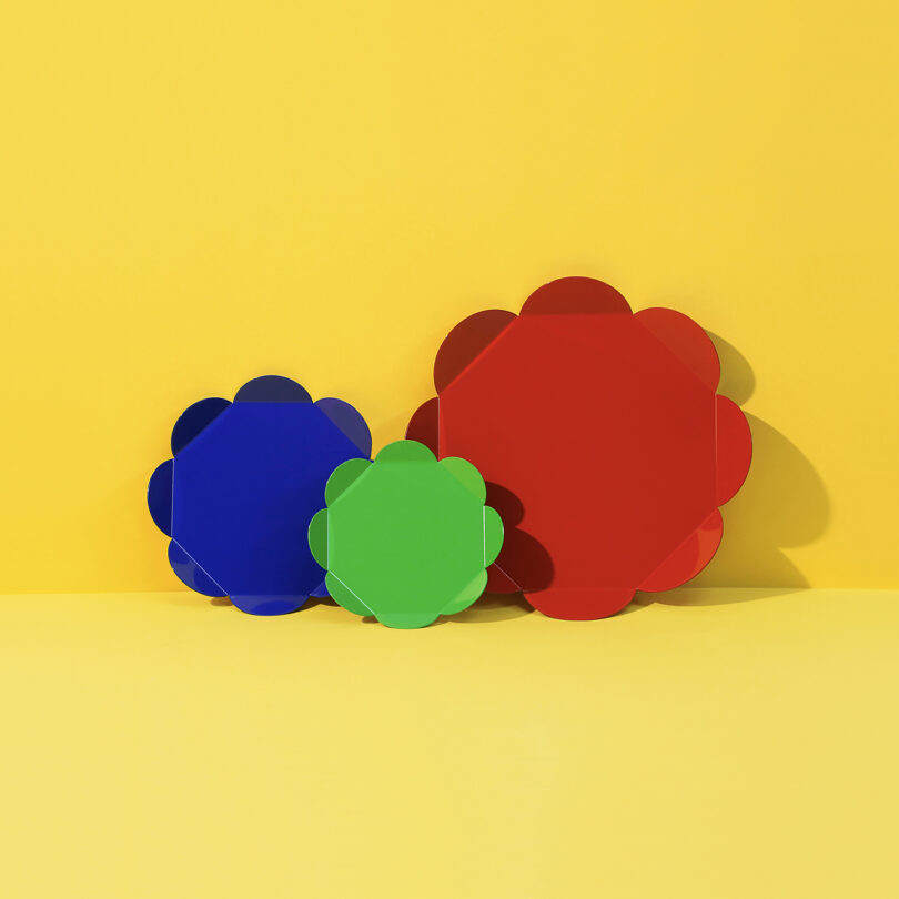 Tres objetos con forma de flor en azul, verde y rojo, ordenados por tamaño sobre un fondo amarillo sólido: una opción llamativa en la guía de regalos 2025.