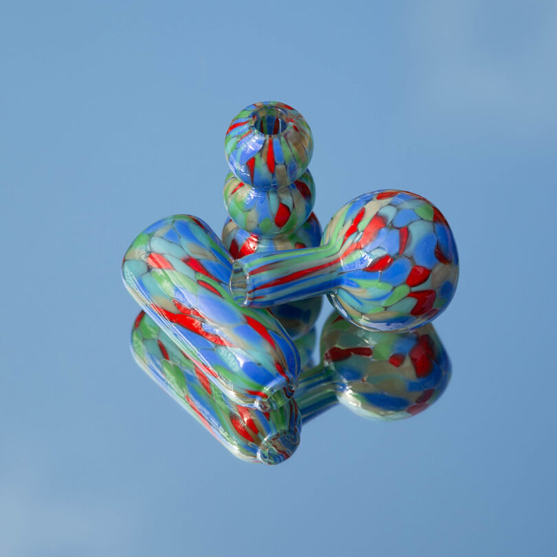 Tres jarrones de vidrieras con patrones rojos, verdes y azules se exhiben sobre una superficie azul reflectante: una opción vibrante para su guía de regalos 2025.