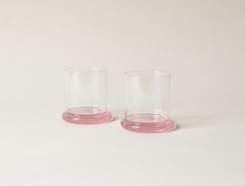 Dos vasos transparentes con bases rosas colocados uno al lado del otro sobre un fondo neutro.