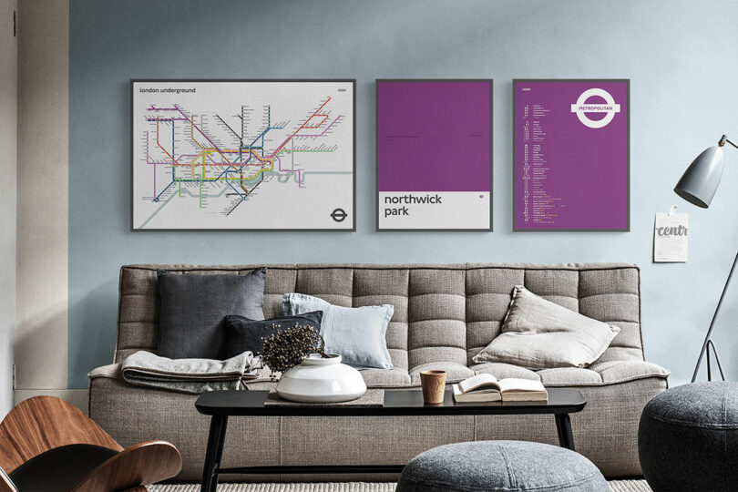 A modern living room with a grey sofa, cushions, a lamp, and three framed London Underground-themed posters on a light blue wall—a perfect setting for any Gift Guide enthusiast.