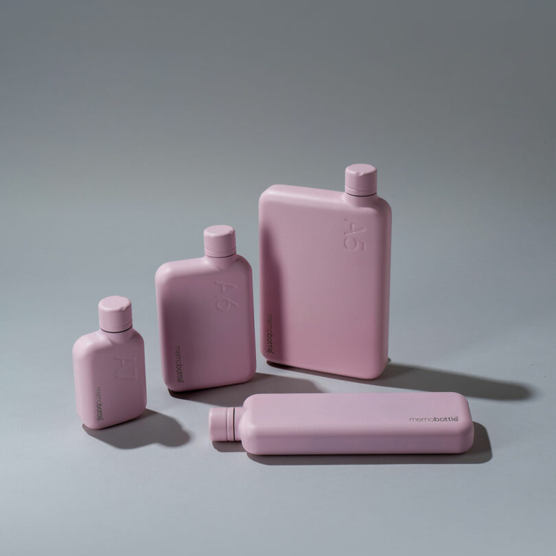 Four matte pink rectangular water bottles of varying sizes are arranged on a gray surface, with three standing upright and one lying flat—a stylish option perfect for any Gift Guide.