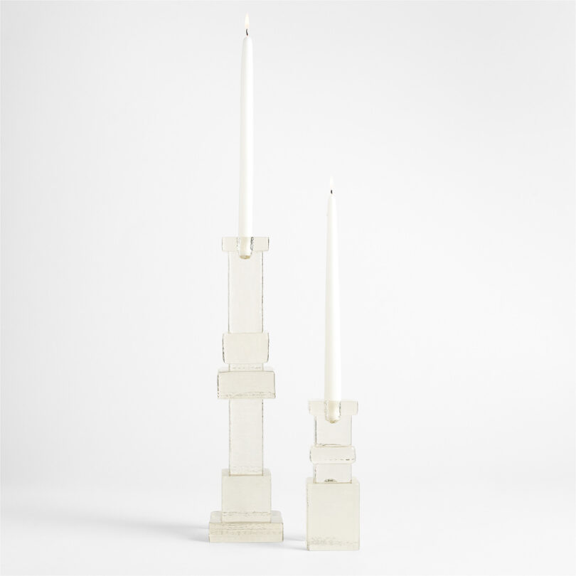 Two white taper candles in modern, geometric white candlesticks of different heights against a plain white background—an elegant addition to any space and a stylish pick for your Gift Guide 2025.