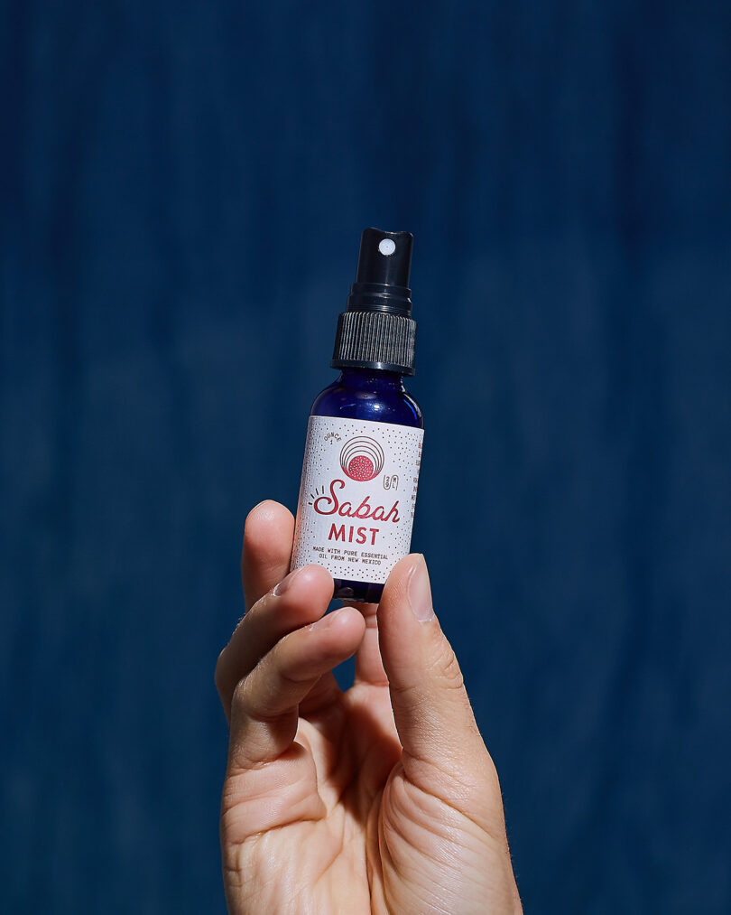 A hand holds a small blue spray bottle labeled "Sabah Mist" against a dark blue background—an elegant pick for any 2025 Gift Guide.