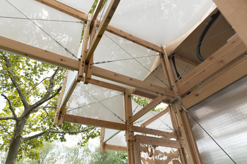 Vista de cerca de la estructura de madera con cables metálicos y paneles de dosel blancos ubicados al aire libre bajo vegetación.