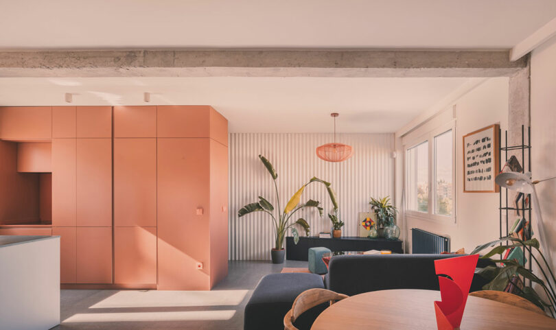 El moderno espacio habitable cuenta con gabinetes color melocotón, asientos grises, grandes plantas de interior y mucha luz natural que entra por los amplios ventanales.