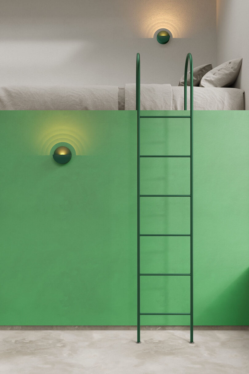 A green ladder leads up to a lofted bed with gray bedding, set against a green wall with two round wall lights, one above and one below.