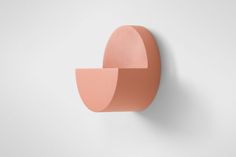 A minimalist, semicircular, pink wall shelf with a smooth matte finish mounted on a white wall.