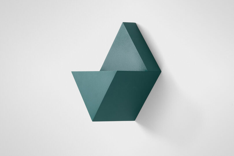 A geometric, wall-mounted dark green shelf with angular shapes and clean lines against a plain white background.