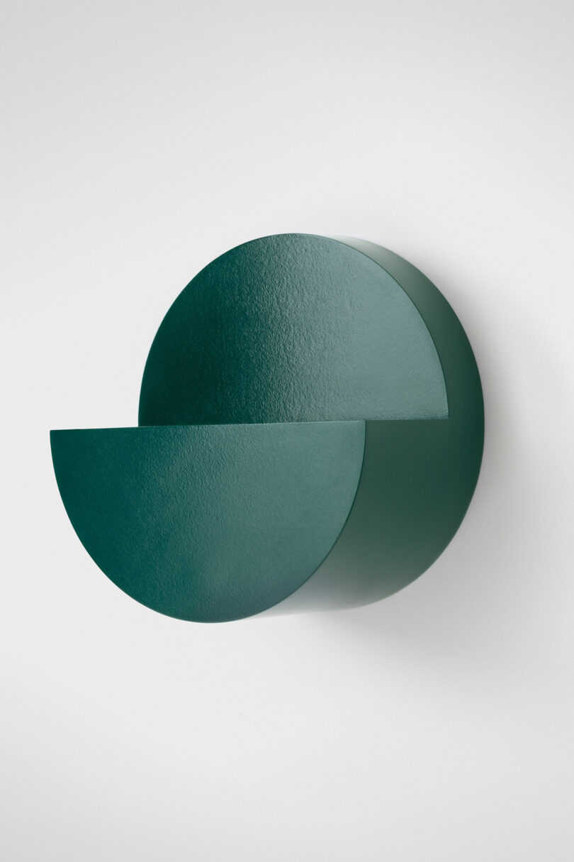 A green wall-mounted fixture with two overlapping semicircular shapes against a white background.