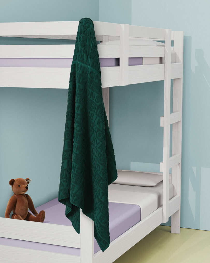 White bunk bed with lavender bedding, a green textured blanket hanging from the top bunk, and a brown teddy bear sitting on the lower bed in a minimal, pastel-colored room.
