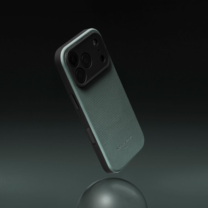 A smartphone in a green textured protective case is suspended above a gray sphere against a dark gradient background.