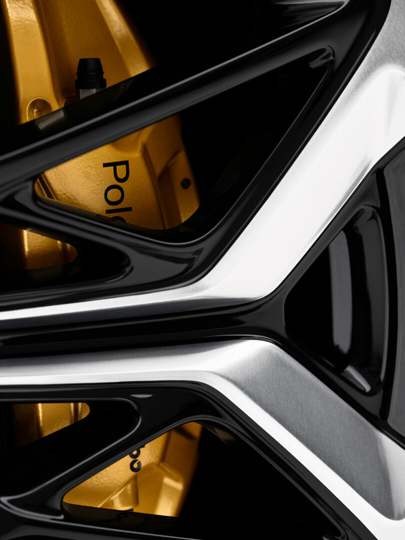 Primer plano de la llanta de un automóvil con un acabado metálico plateado y negro, que muestra una pinza de freno amarilla con la inscripción 