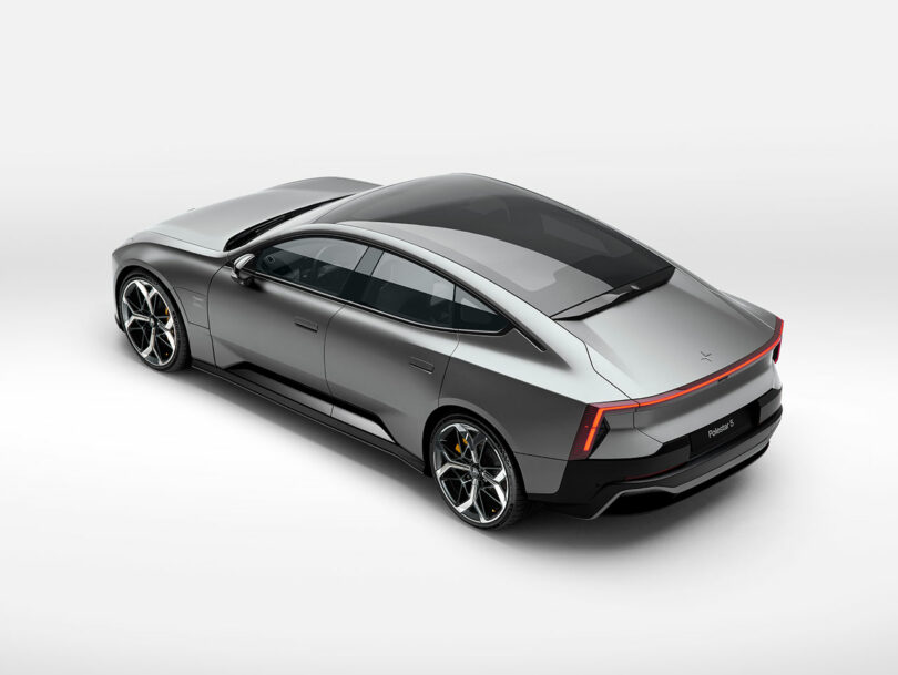 Un sedán eléctrico plateado con un elegante diseño aerodinámico, techo negro, cristales tintados y modernas llantas de aleación, fotografiado desde un ángulo alto sobre un fondo blanco puro.