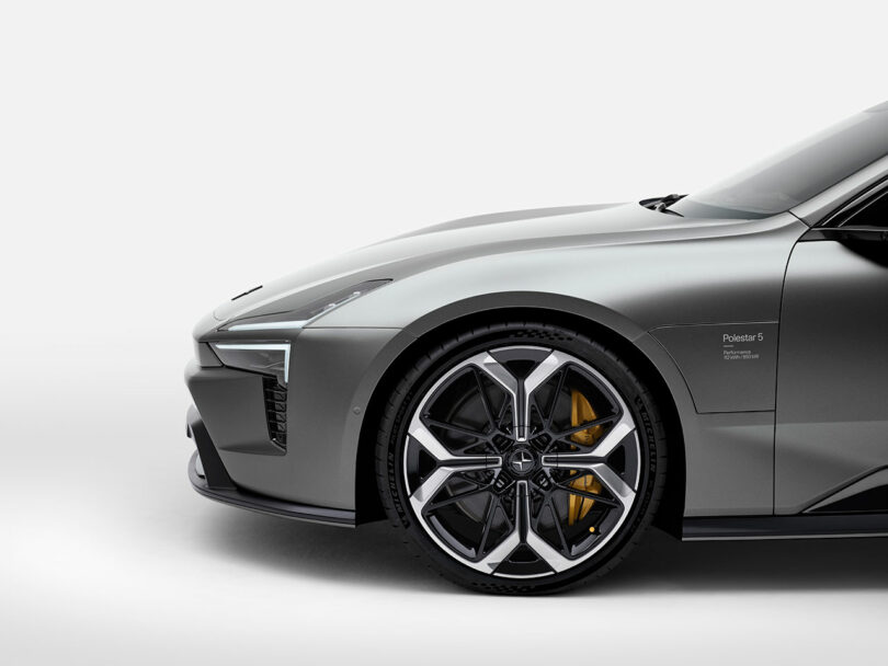 Vista frontal de un automóvil eléctrico Polestar 5 gris, que muestra sus ruedas, neumáticos y diseño de faros sobre un fondo blanco puro.