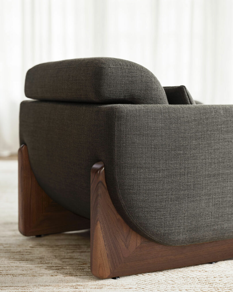 A close-up of a modern dark gray upholstered armchair with wooden legs and a textured fabric finish, placed on a light-colored rug.