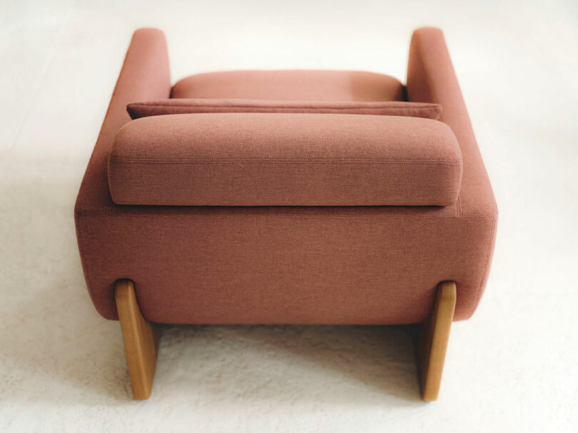 A modern armchair with pink upholstery and wooden legs, viewed from the back on a light-colored floor.