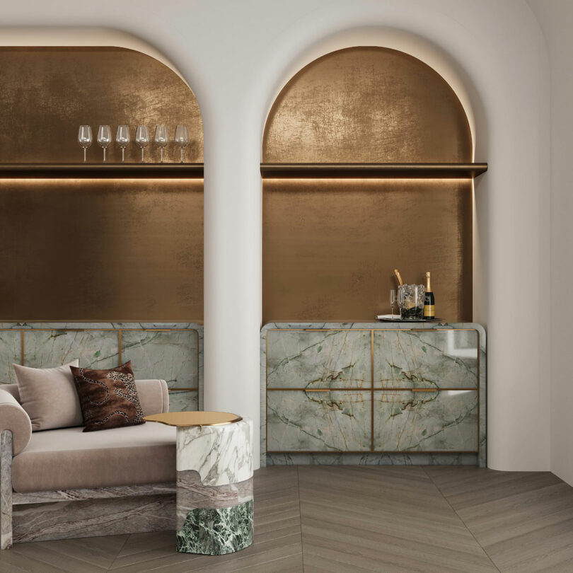 A modern interior features a marble bar with a champagne bottle and glasses, a beige sofa, and metallic gold accents under two arched alcoves.