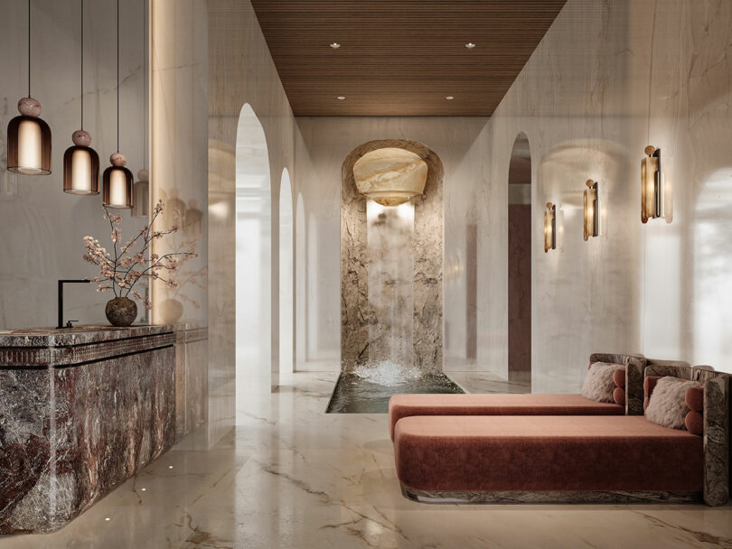 A modern, marble-lined spa interior featuring a small waterfall, lounge chairs with pink cushions, pendant lights, and decorative wall sconces.