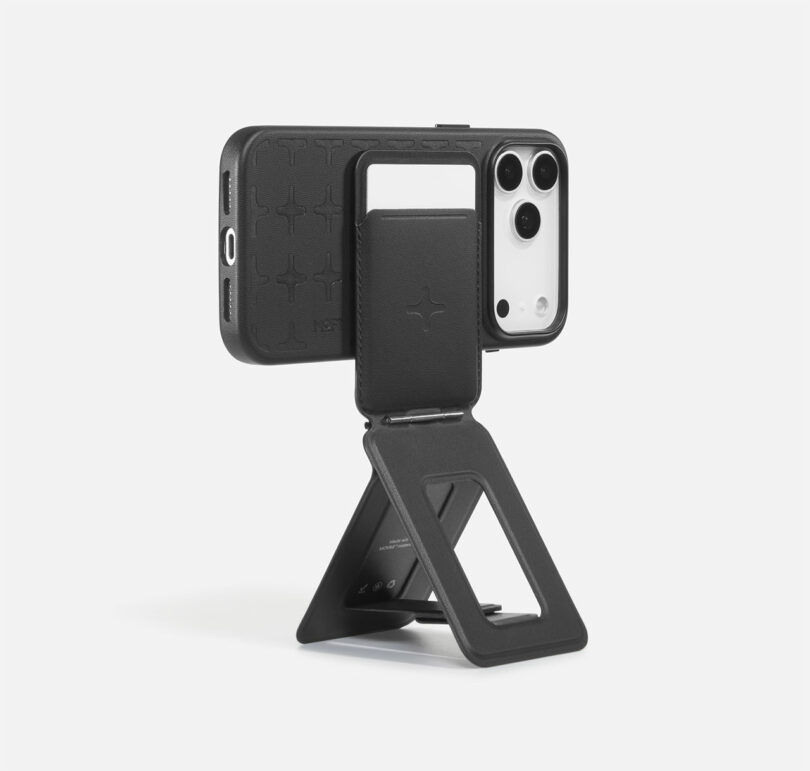 A black phone case with a built-in stand and card holder is shown holding a white smartphone upright on a white background.