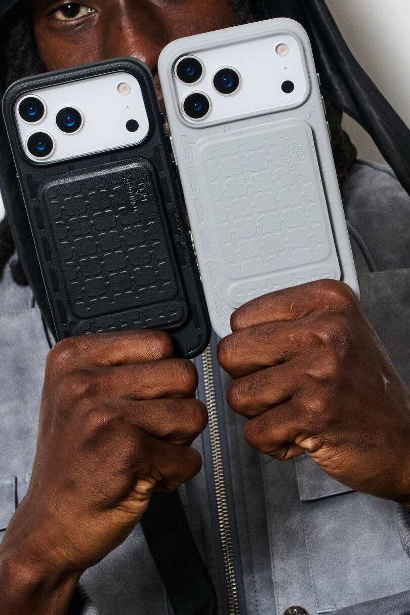 A person holds up two smartphones with rugged cases, one black and one white, partially covering their face.