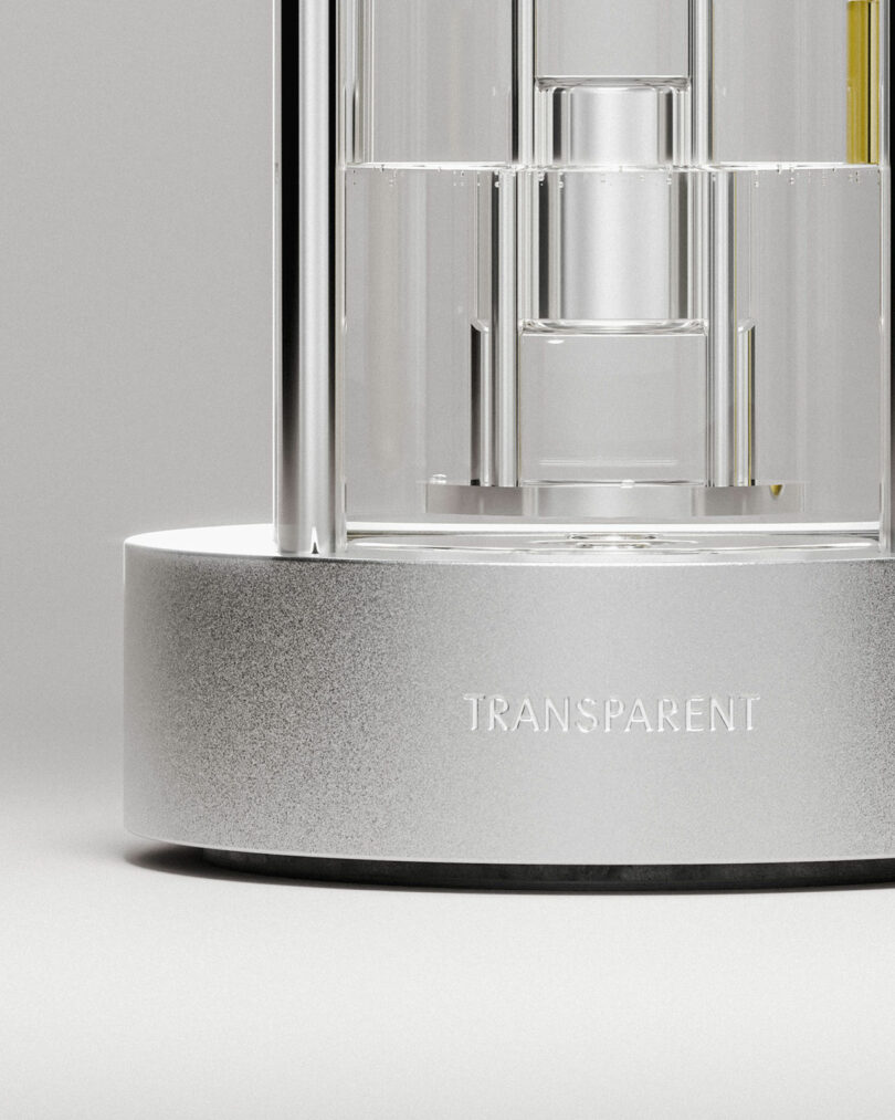 Close-up of a modern, cylindrical glass and metal aroma diffuser on a metallic base with the word "TRANSPARENT" engraved on it.
