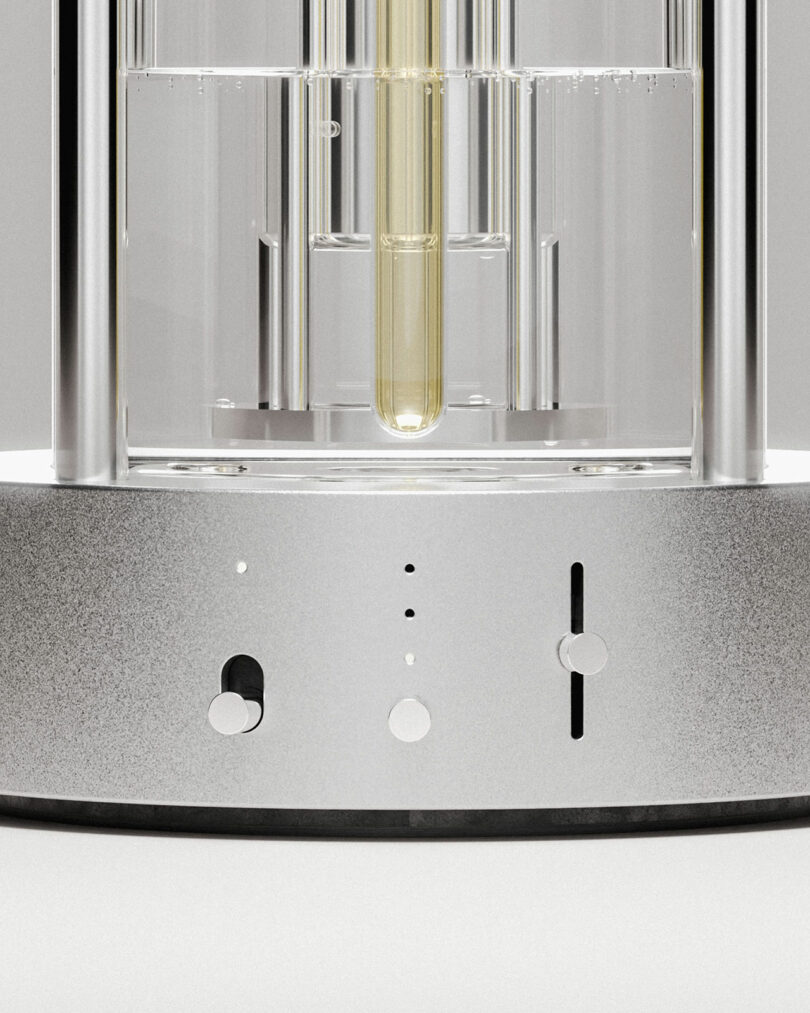 Close-up of an Aroma Diffuser's metallic base featuring switches, buttons, and a central glass tube filled with a yellowish liquid.