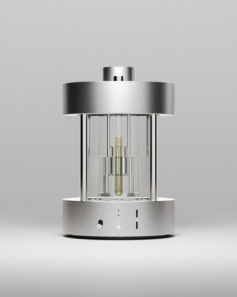 A cylindrical, metallic and glass device with a transparent center chamber and a metallic top and base, displayed against a plain light background.