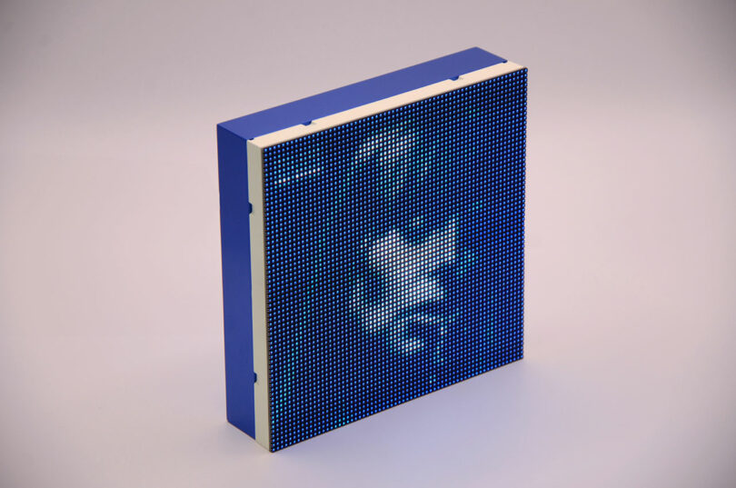 Un panel de visualización LED rectangular azul muestra una tenue imagen pixelada de un rostro humano en su frente.