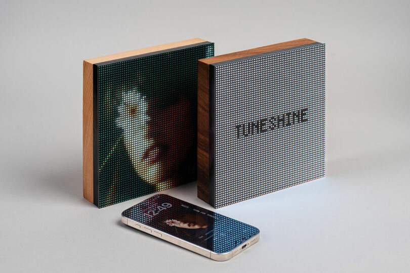 Dos pantallas digitales cuadradas con marco de madera, una que muestra arte pixelado y la otra que lee texto. "piedra sonora," Colóquelo detrás del teléfono inteligente boca arriba.