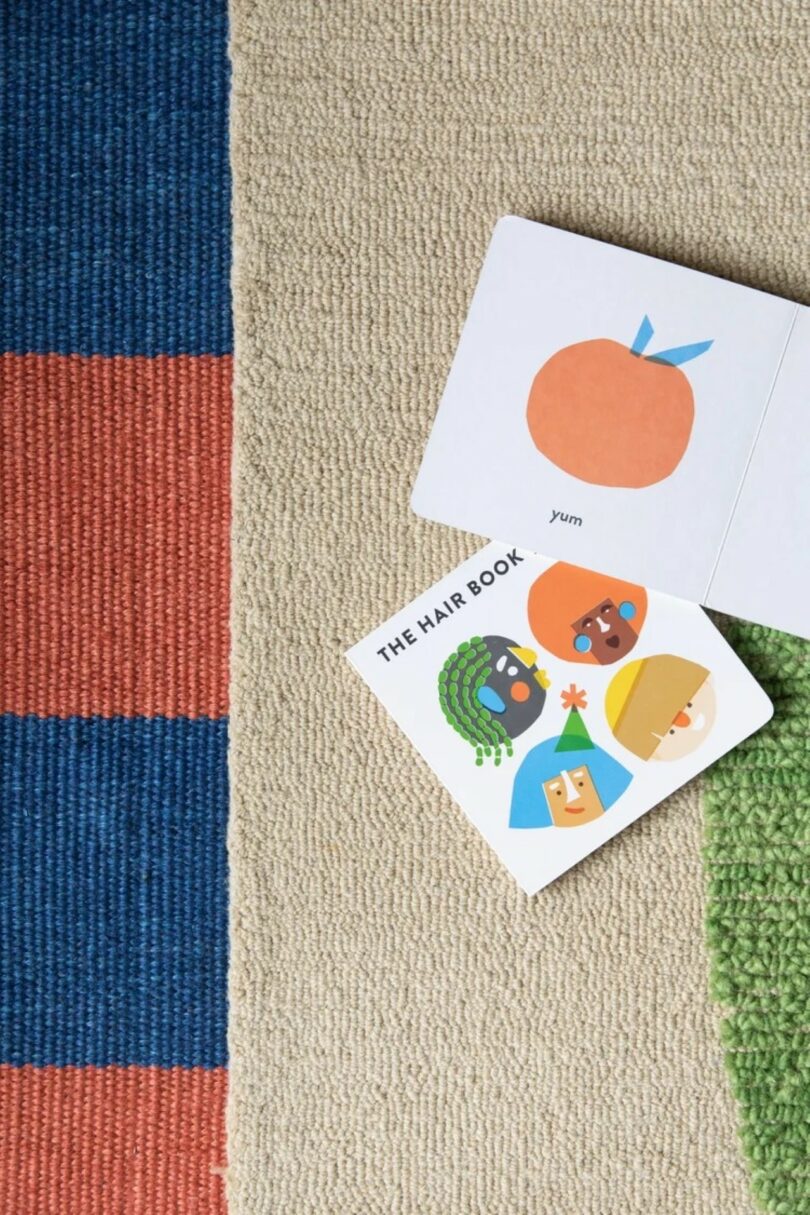 Dos libros infantiles abiertos y colocados sobre una alfombra texturizada; uno muestra frutas de color naranja y el otro muestra rostros con diferentes peinados