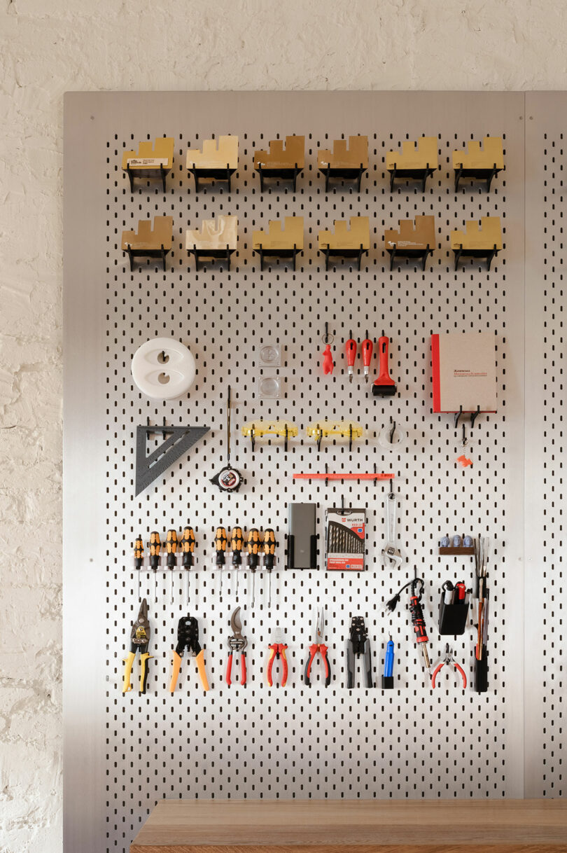 A pegboard mounted on a wall displays various hand tools, including pliers, screwdrivers, a ruler, and storage boxes, neatly organized in rows.