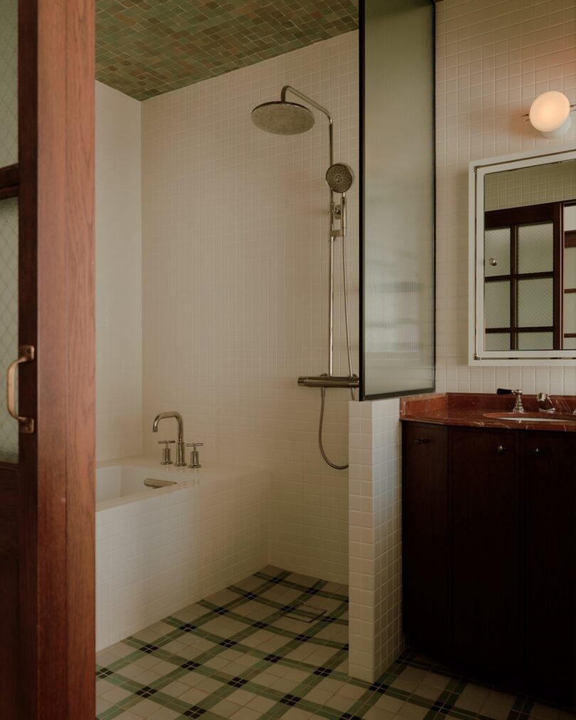 El baño minimalista cuenta con una cabina de ducha, paredes con azulejos blancos, una bañera, un tocador de madera oscura con lavabo y un piso de baldosas con diseño de cuadros.