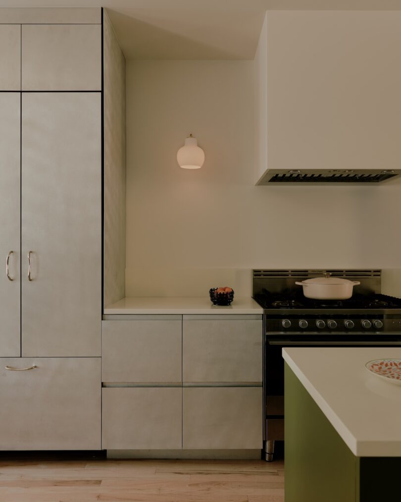 Cocina moderna con armarios de color gris claro, estufa con ollas blancas, lámpara de pared y un pequeño cuenco de bayas sobre la encimera.