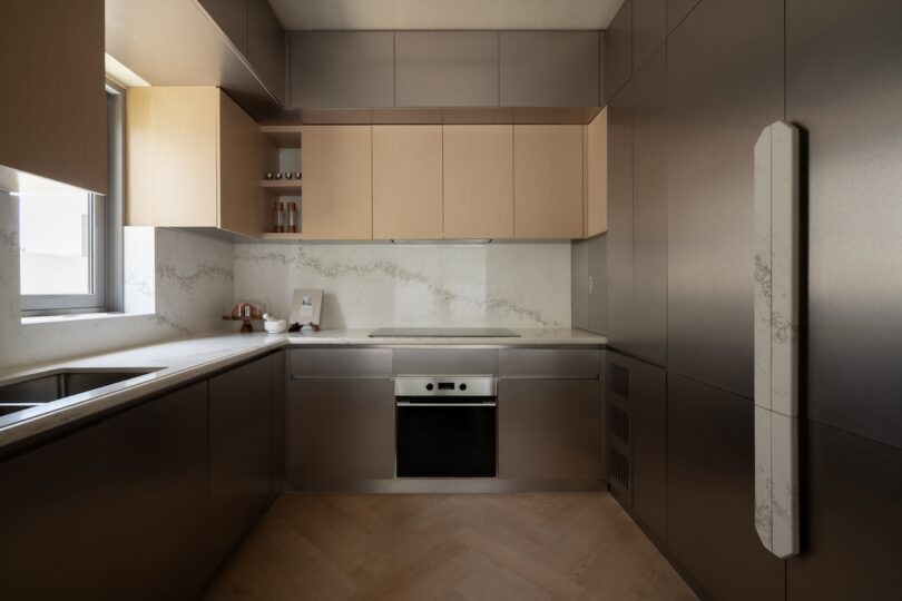 La cocina moderna y minimalista cuenta con gabinetes de madera clara, superficies de acero inoxidable, horno empotrado, placa para salpicaduras de mármol y piso de madera en forma de espiga.