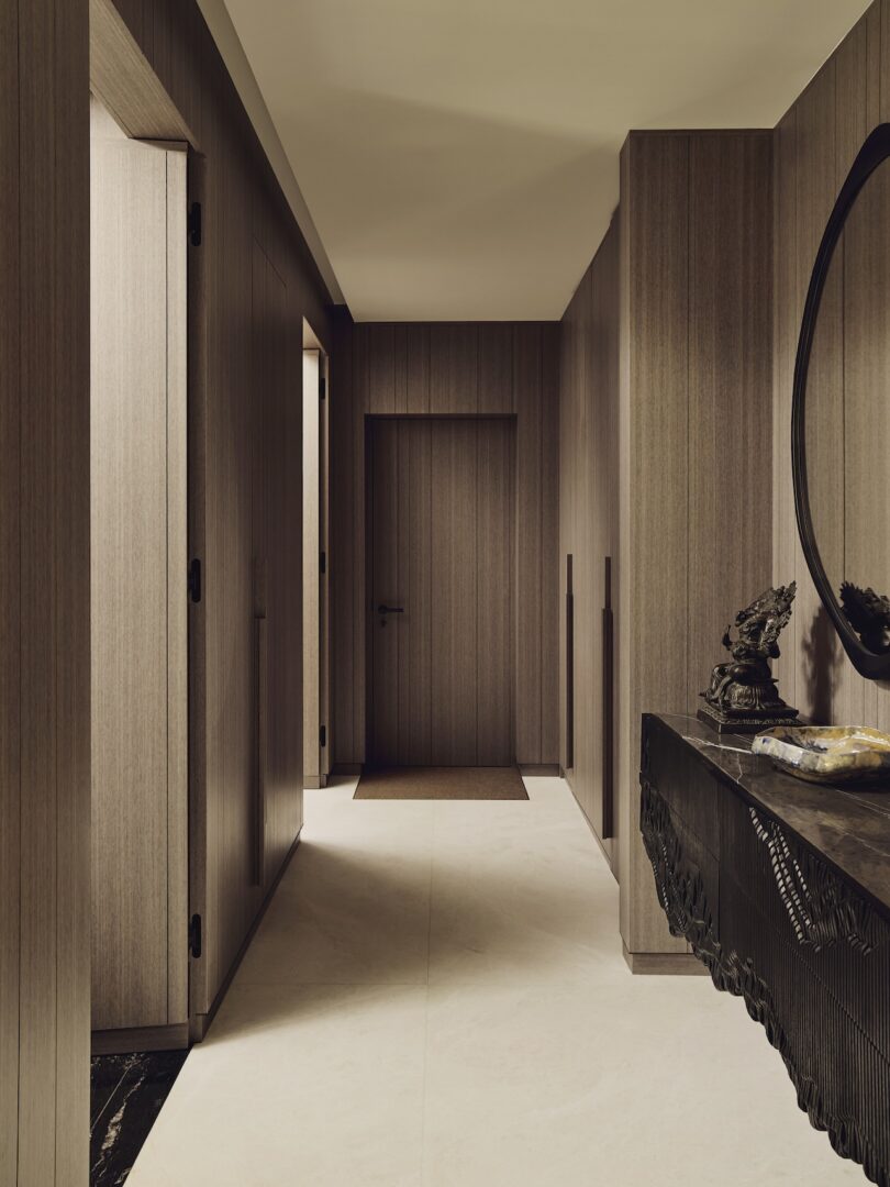 Pasillo moderno con paredes revestidas de madera, una puerta cerrada al final y una mesa consola oscura con detalles decorativos a la derecha.