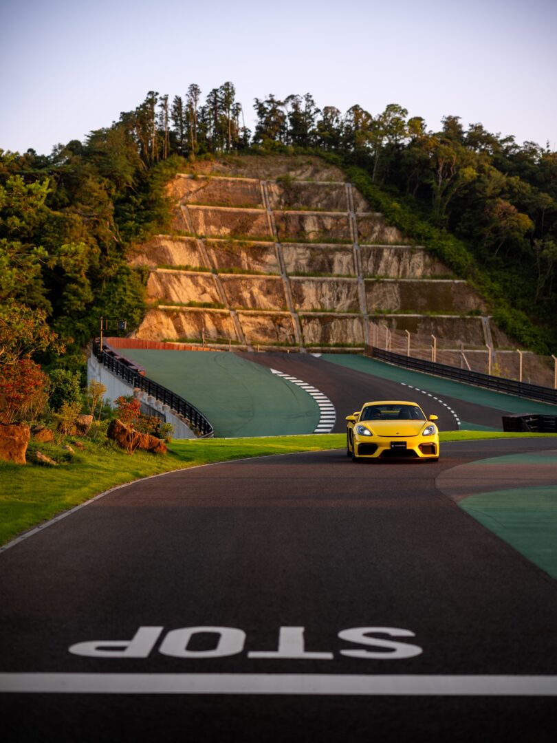 Un coche deportivo amarillo circula por una pista cerca de una línea de parada pintada sobre un fondo de empinadas colinas y árboles en terrazas.