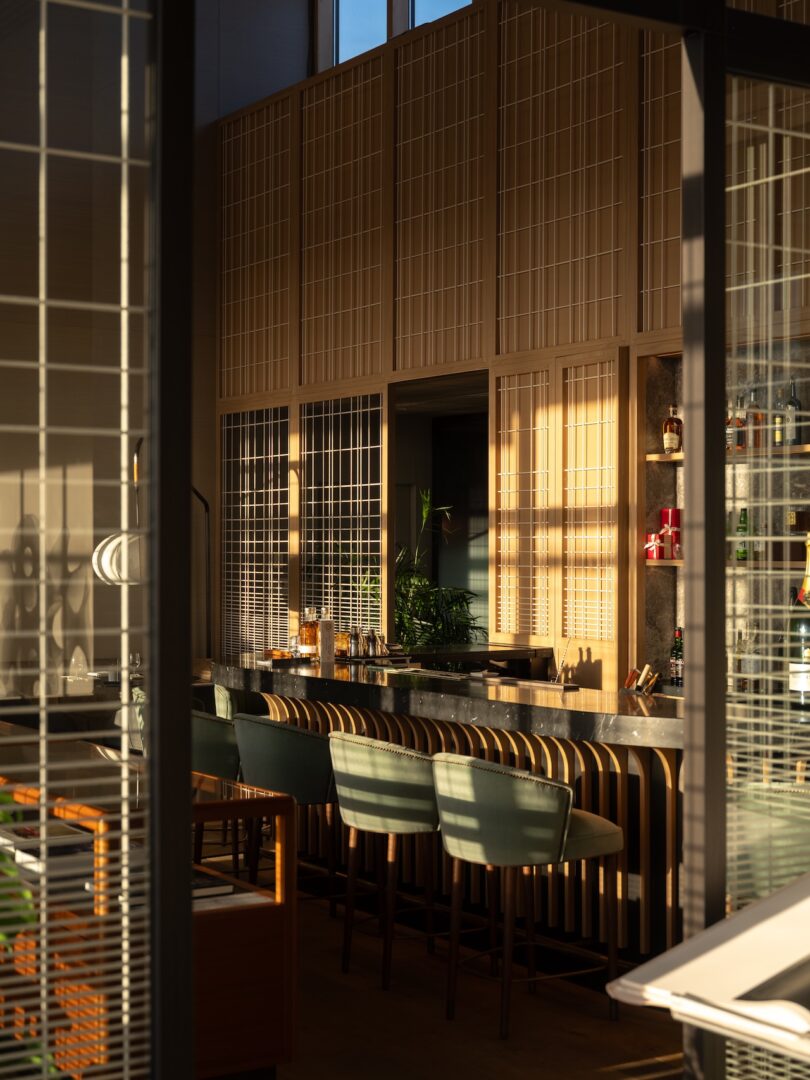 La moderna zona del bar cuenta con taburetes verdes, encimeras de mármol, paneles de madera y luz del sol que entra a través de ventanas altas.