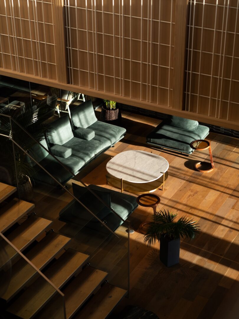 La moderna sala de estar cuenta con un sofá verde, una mesa de centro de mármol blanco, pisos de madera y la luz del sol que entra a través de paneles verticales de ventanas.