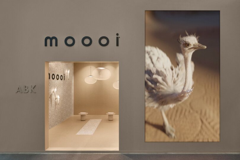 La moderna entrada de la tienda presenta carteles de Moooi, interiores en tonos neutros, luces tipo globo y una gran imagen de avestruz en la pared a la derecha.