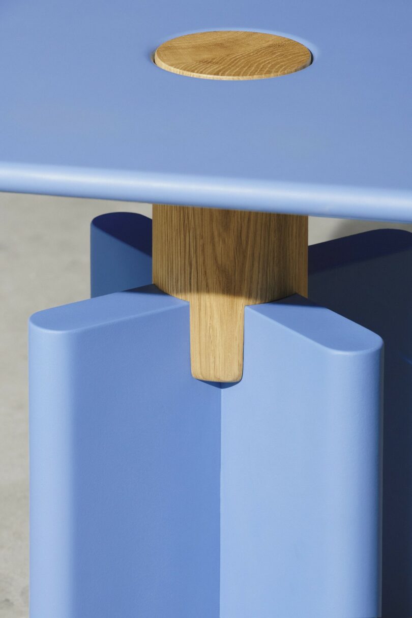 Primer plano de una mesa azul con incrustaciones redondas de madera y soportes de madera que conectan las patas, diseño geométrico moderno