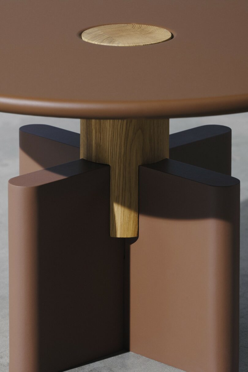 Una mesa redonda de color marrón con una incrustación circular de madera en la parte superior y una base geométrica de madera y marrón colocada sobre un suelo de hormigón liso.
