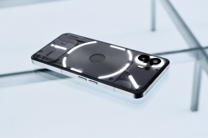 Un teléfono inteligente con parte trasera transparente se coloca sobre una mesa de cristal, lo que permite ver los componentes internos y la tira de LED brillante.