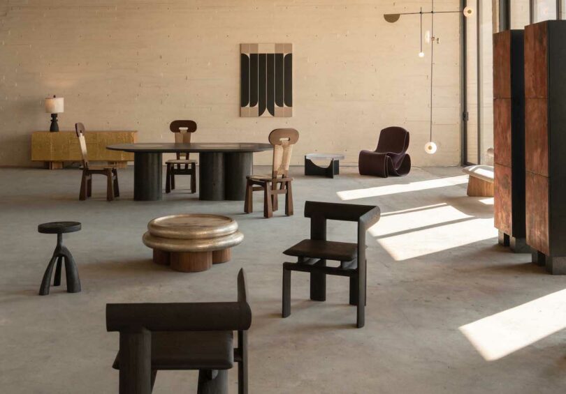 El interior minimalista del loft presenta muebles modernos y eclécticos que incluyen sillas de madera oscura, mesas redondas, sillones esculturales, arte abstracto en las paredes y una suave luz natural.